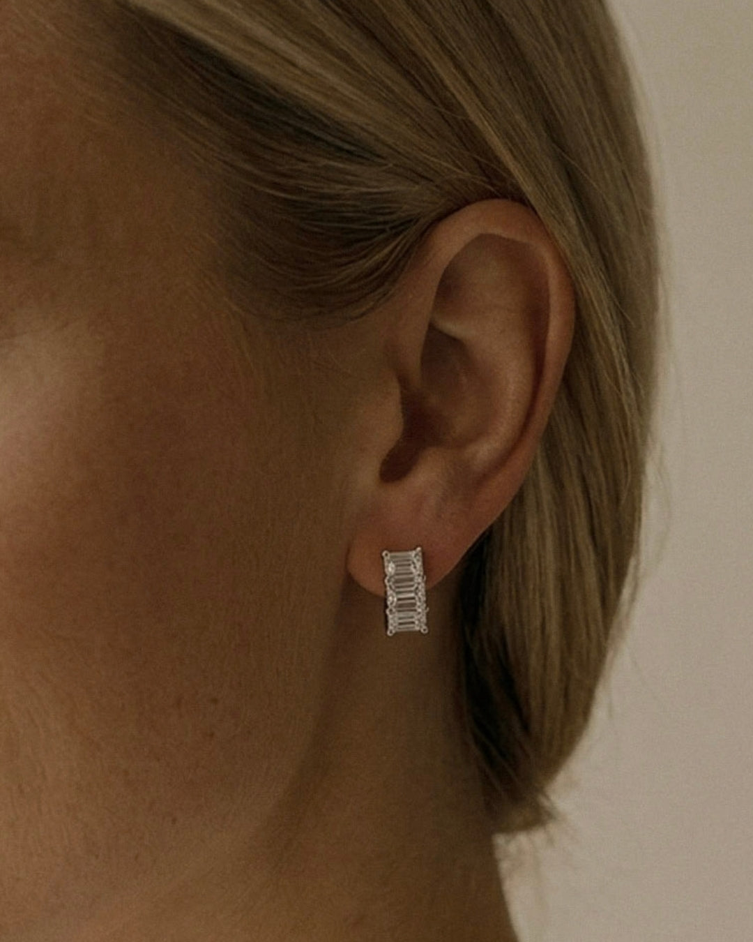 Lab grown emerald cut diamond huggie earrings with three diamonds per hoop in 14K white  gold on ear